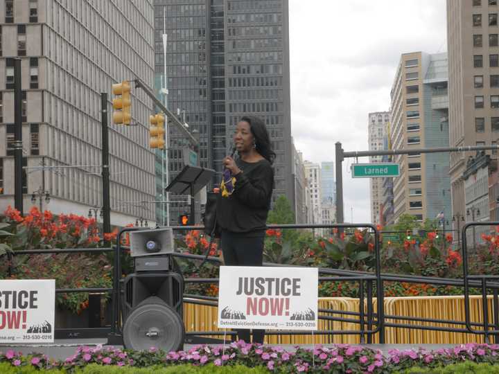 Black woman on stage, speaking into a microphone. 